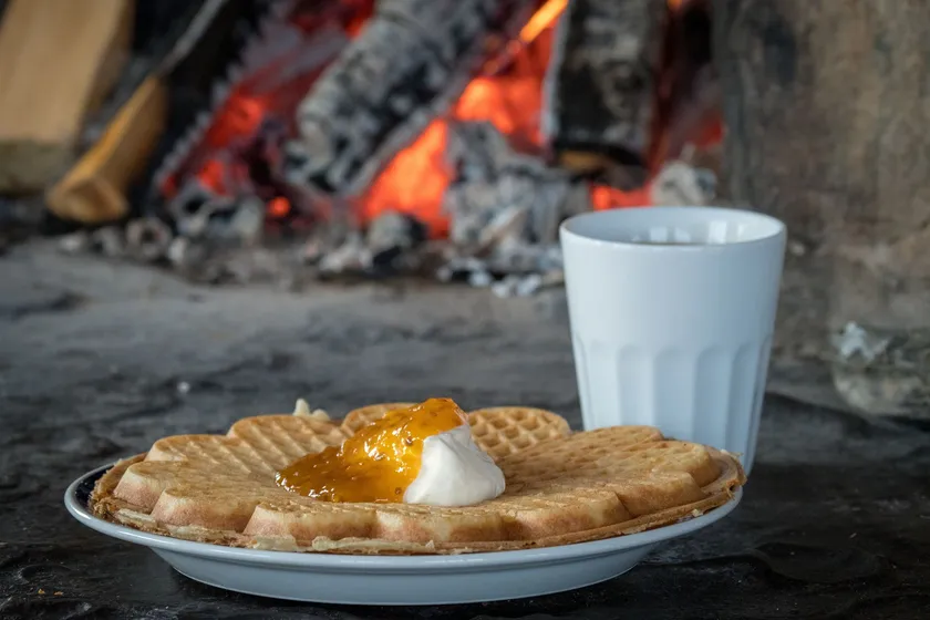 Tallrik med våffla och kaffekopp, brasa i bakgrunden.
