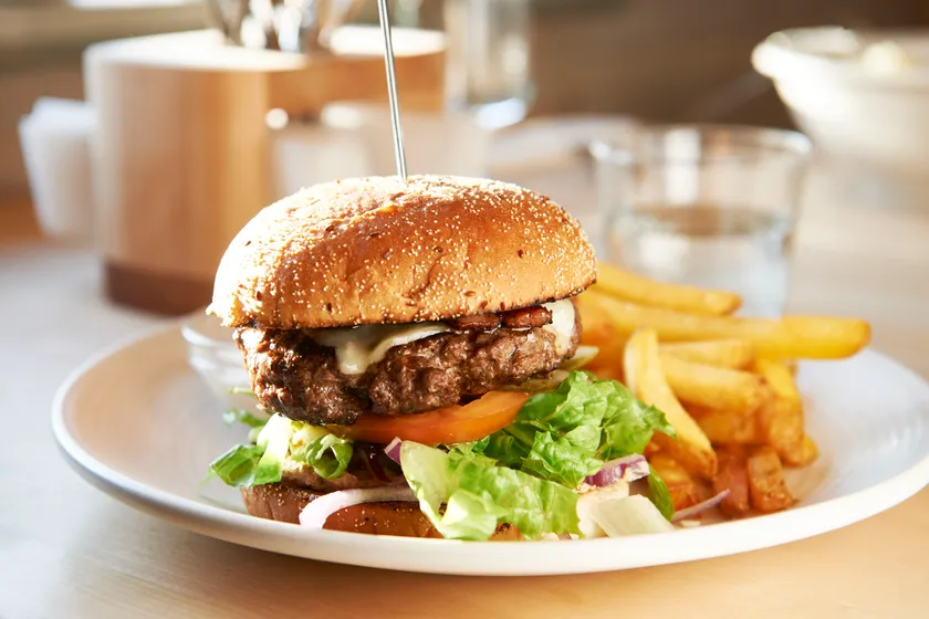 Tallrik med hamburgare med sallad, dressing och pommes.