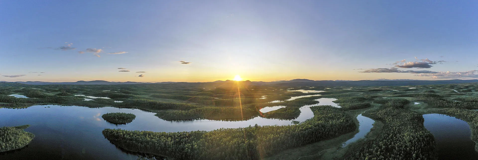 Flygfoto över skog och vatten i soluppgång.