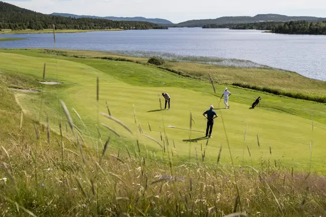Tre personer spelar golf längs en fjällsjö