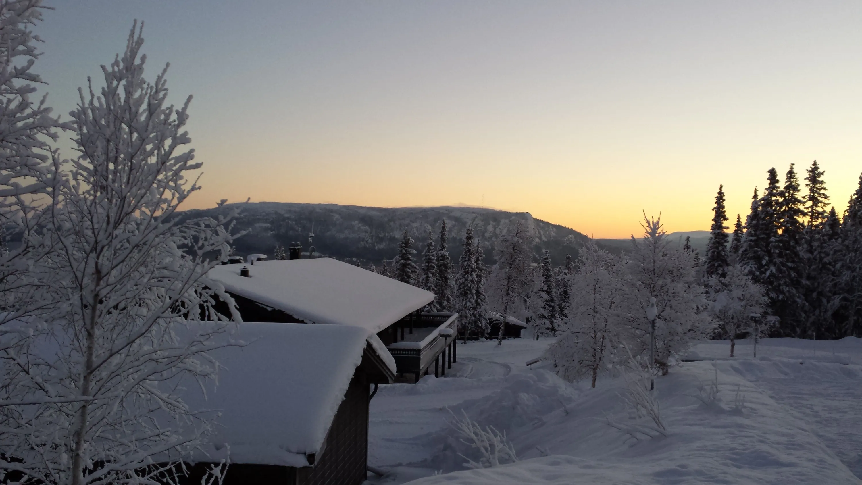 Snötäckta stugor i soluppgång, med utsikt mot Funäsdalsberget.
