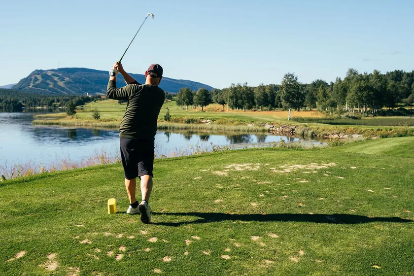 Person spelar golf med fjällen i bakgrunden