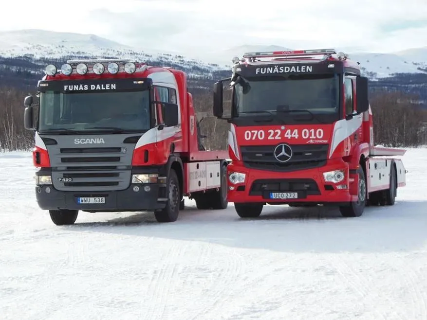 Två bärgningsbilar med fjäll i bakgrunden