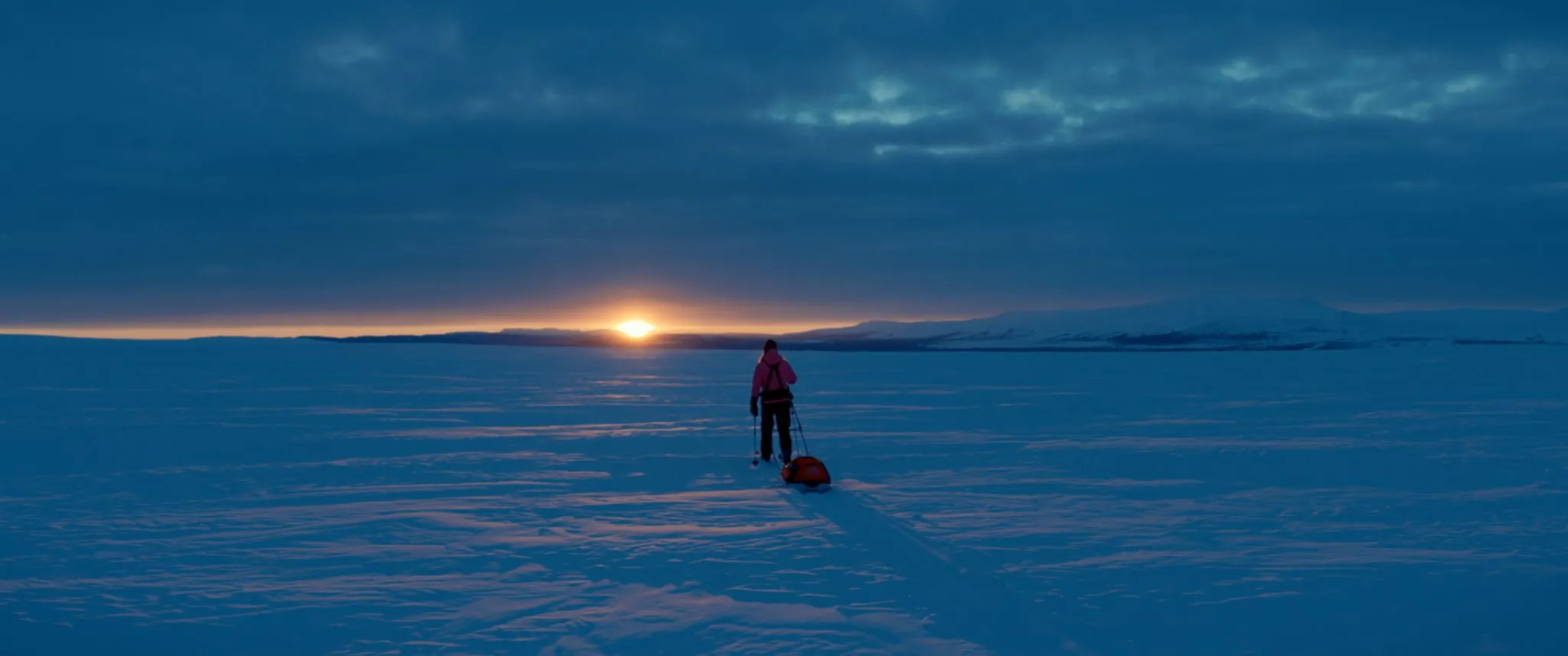 Person på skidor med pulka efter, snötäckt fjällandskap.