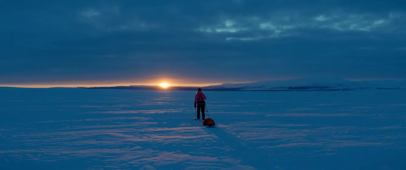 Person på skidor med pulka efter, snötäckt fjällandskap.