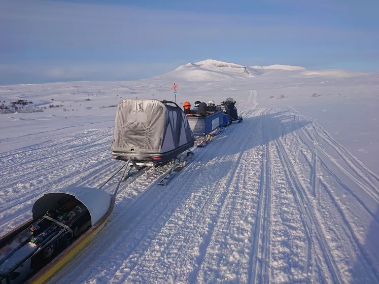Skoter som drar flera slädar efter sig ut på fjället.